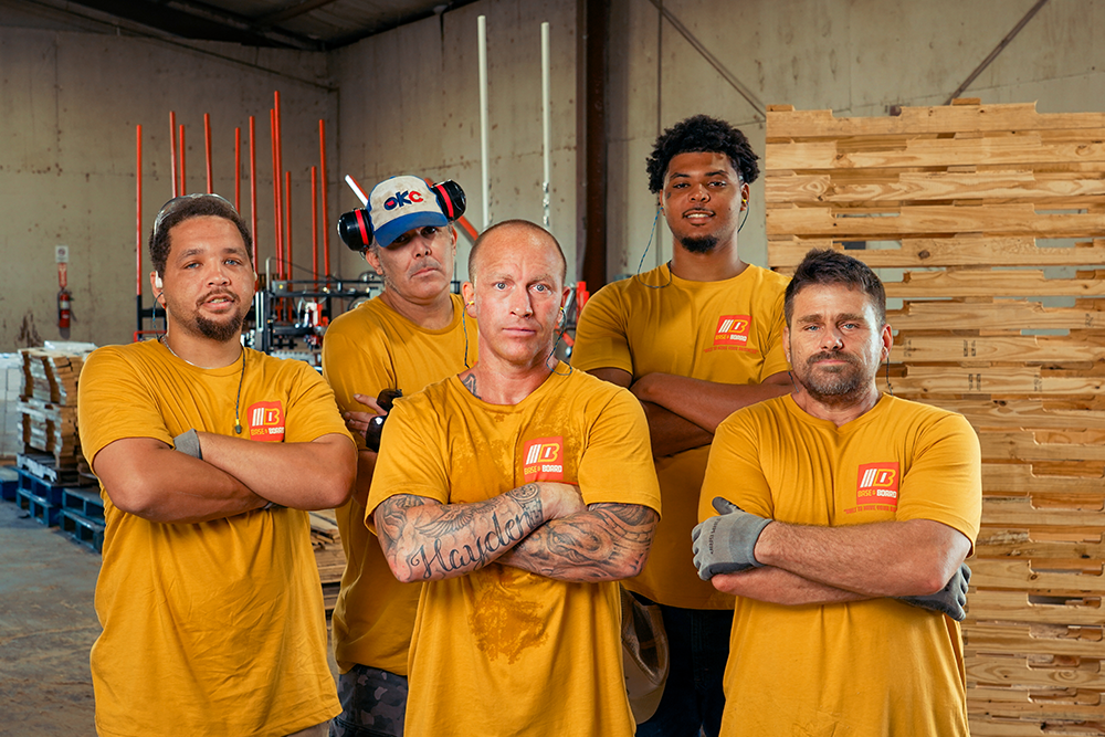 Group of workers in warehouse with pallets stacked behind them.