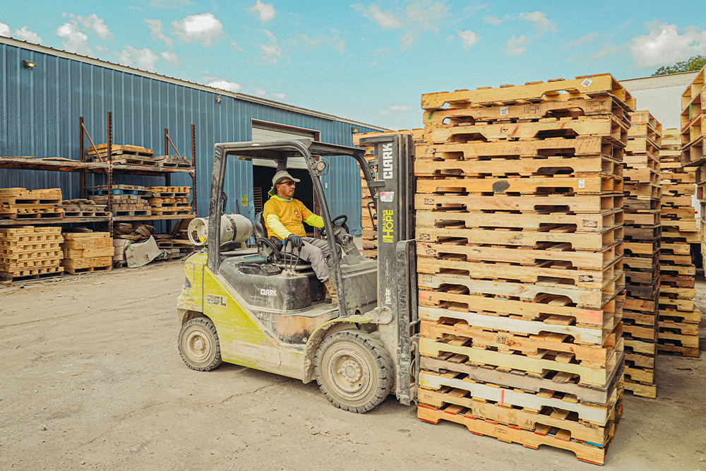 Forklift stacking wooden pallets at a loading dock. Pallets are stacked.