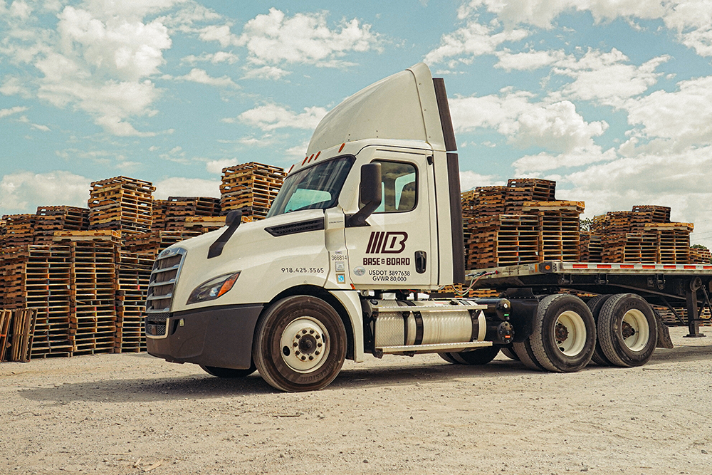 Semi delivering pallets at loading dock with stacks behind.
